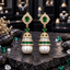 Pair of gold-tone jhumka earrings with green oval accents, clear sparkling details and large white pearl-look drops.