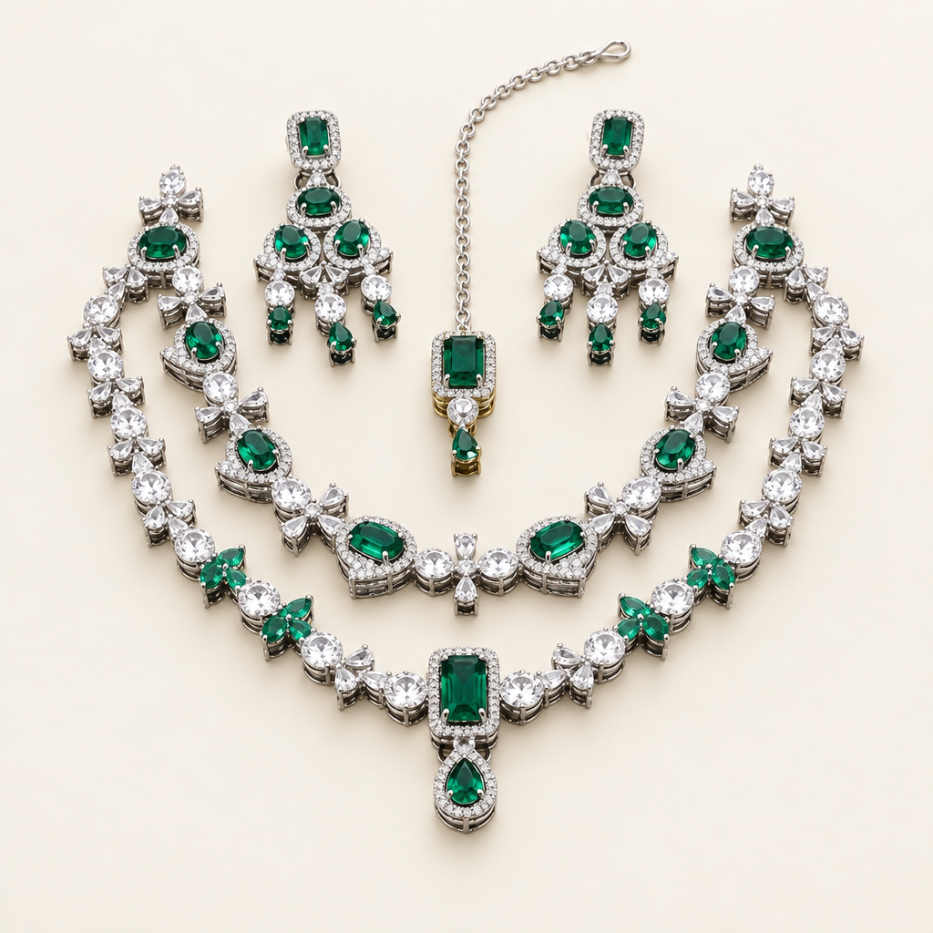 Emerald-green AD bridal jewelry set with layered silver-tone necklaces, matching earrings, and maang tikka on an ivory studio background