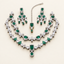 Emerald-green AD bridal jewelry set with layered silver-tone necklaces, matching earrings, and maang tikka on an ivory studio background