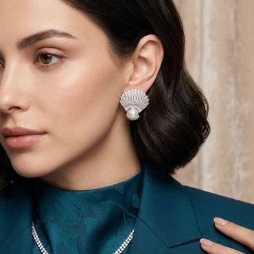 Micro Pavé CZ Seashell Faux Pearl Stud Earrings in gold-tone plating flat lay on dark grey mirror surface showing pair of fully CZ encrusted fan seashell studs with large round faux pearl in CZ cradle at base with mirror reflections below and grey silk backdrop