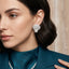 Micro Pavé CZ Seashell Faux Pearl Stud Earrings in gold-tone plating flat lay on dark grey mirror surface showing pair of fully CZ encrusted fan seashell studs with large round faux pearl in CZ cradle at base with mirror reflections below and grey silk backdrop