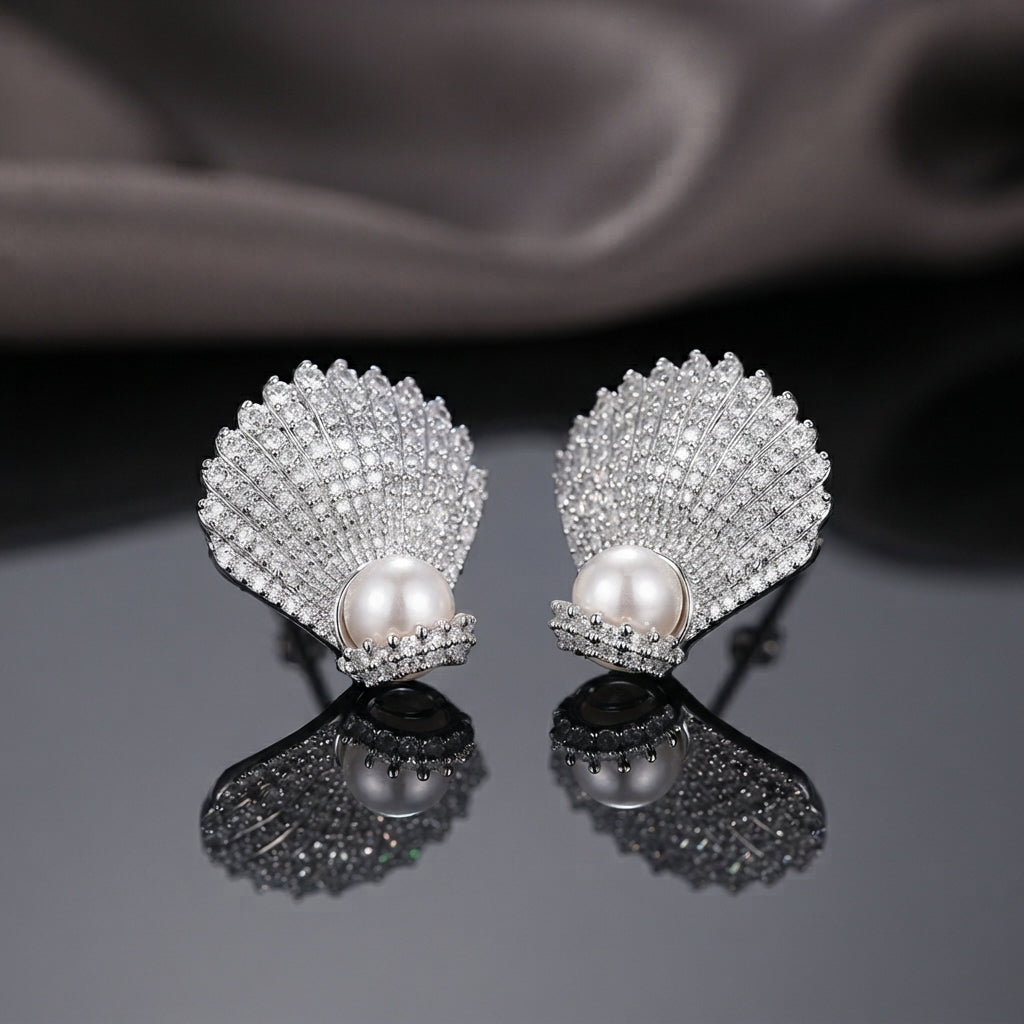 Micro Pavé CZ Seashell Faux Pearl Stud Earrings in gold-tone plating worn on model ear with beige warm background and cream outfit showing full CZ encrusted seashell design with large oval pearl at base