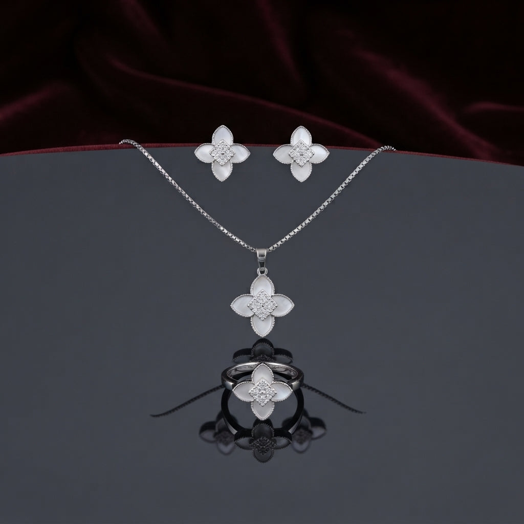 Mother of Pearl Clover Flower CZ Pavé Pendant Necklace Earrings and Ring Set in gold-tone flat lay on grey mirror surface with burgundy velvet backdrop showing 3-piece set with 4-petal clover flower design in white mother of pearl petal inlay and white CZ micro-pavé center cluster with mirror reflection