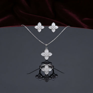Mother of Pearl Clover Flower CZ Pavé Pendant Necklace Earrings and Ring Set in gold-tone flat lay on grey mirror surface with burgundy velvet backdrop showing 3-piece set with 4-petal clover flower design in white mother of pearl petal inlay and white CZ micro-pavé center cluster with mirror reflection