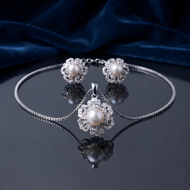 Pearl Center CZ Multi-Layer Floral Halo Pendant Necklace and Earrings Set in gold-tone flat lay on grey mirror surface with burgundy velvet backdrop showing 2-piece set with large cream pearl center in dense multi-layer white CZ floral sunburst halo pendant necklace and matching stud earrings with mirror reflection