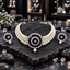 Cream pearl-look multi-strand choker with a round black-accent medallion, clear concentric borders, a floral centre and pearl-look drop, displayed with matching round drop earrings on dark slate.
