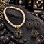 Cream pearl-look beaded necklace with black oval pendant, matching earrings and ring, surrounded by black decorative accents on dark slate.