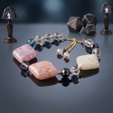 Statement necklace with large pale pink and cream square-shaped beads, clear, dark, and iridescent-looking accents, and gold-tone chain details.