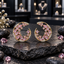 Pair of gold-tone open crescent earrings with pink leaf-shaped and round accents, clear sparkling details, displayed on dark stone.
