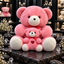 Two pink-and-white teddy bears with red ribbon bows, a larger seated bear behind a smaller matching bear with a red heart-and-eye detail.