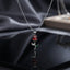 Red CZ Rose Flower Stem Pendant Necklace in silver-tone flat lay on black mirror surface with dark grey silk backdrop showing 3D rose bud pendant with faceted red CZ petals and silver engraved stem with green enamel leaf accent and round bezel CZ on silver cable chain with mirror reflection below