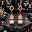 Pair of gold-tone jhumka earrings with red oval accents, clear sparkling details and large white pearl-look drops.