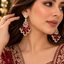 Red and pale pink teardrop chandelier earrings with gold-tone settings, worn with an embroidered outfit.