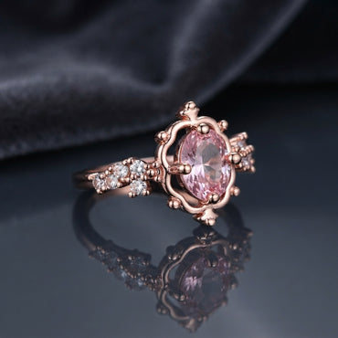 Rose Gold Oval Morganite Crown Solitaire Ring in blush pink CZ on dark mirror surface with grey silk backdrop showing 18K rose gold-tone ornate open scrollwork crown setting holding faceted oval blush pink morganite CZ centre stone with 3+3 round white CZ shoulder clusters with mirror reflection below