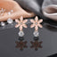 Rose Gold Pink Enamel Flower CZ Drop Stud Earrings pair on black mirror surface with scattered loose CZ stones and grey silk fabric backdrop showing rose gold-tone 5-petal daisy plumeria flower stud with blush pink enamel petals gold outlined edges tiny CZ centre and large round brilliant open-bezel white CZ drop with mirror reflections below