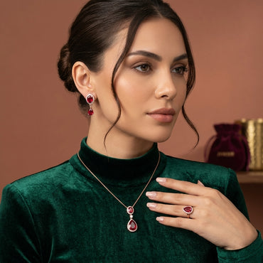 Rose Gold Ruby CZ Oval and Pear Halo Pendant Necklace Drop Earrings and Ring Bridal Set — rose gold-tone 3-piece bridal set with dual oval and pear ruby CZ halo pendant necklace matching drop earrings and large pear ruby CZ halo cocktail ring displayed on black hexagonal tray with burgundy velvet box backdrop