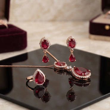 Rose Gold Ruby CZ Oval and Pear Halo Pendant Necklace Drop Earrings and Ring Bridal Set worn by model in emerald green velvet turtleneck showing necklace earrings and ring styling in luxury editorial setting