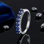 Silver-Tone 7-Stone Round Blue Sapphire CZ Half Eternity Adjustable Band Ring on black reflective surface with navy blue velvet pouch and scattered black pebbles backdrop