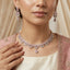 Silver Baguette Fan Scallop CZ Necklace Earrings Tikka Bridal Set in Rose Pink — model wearing rhodium-plated rose pink baguette fan scallop collar necklace with pear CZ center drop, matching 3-drop chandelier earrings and maang tikka, cream silk dupatta editorial backdrop