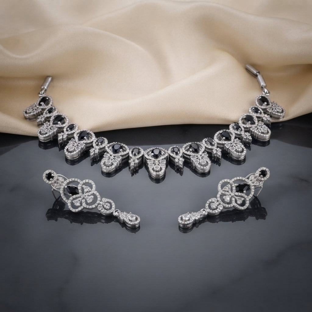 Silver Black and White CZ Art Deco Collar Necklace and Bar Drop Earrings Set — rhodium silver-tone 2-piece Art Deco set with graduating V-motif bib collar necklace featuring oval black CZ white CZ micro-pavé scrollwork and baguette black CZ fringe drops and matching horizontal bar scroll drop earrings displayed on dark mirror surface with cream silk backdrop