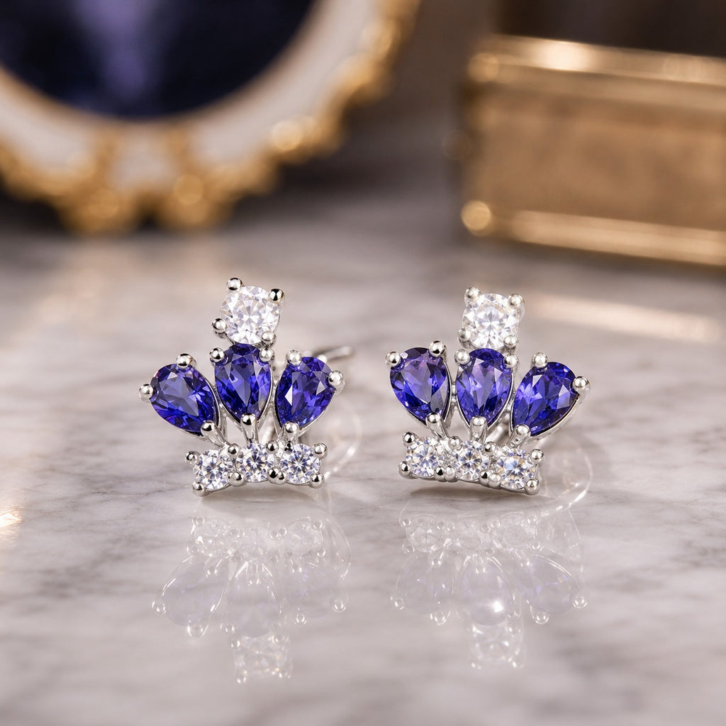 Silver-Tone Blue Sapphire Pear & White CZ Crown Cluster Stud Earrings on grey marble surface with deep navy blue geode and antique gold jewelry box backdrop