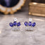 Silver-Tone Blue Sapphire Pear & White CZ Crown Cluster Stud Earrings on grey marble surface with deep navy blue geode and antique gold jewelry box backdrop