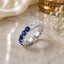 Silver-Tone Blue Sapphire & White CZ Alternating Full Eternity Band Ring on cream marble surface with gold decorative bowl and white baby's breath flowers backdrop