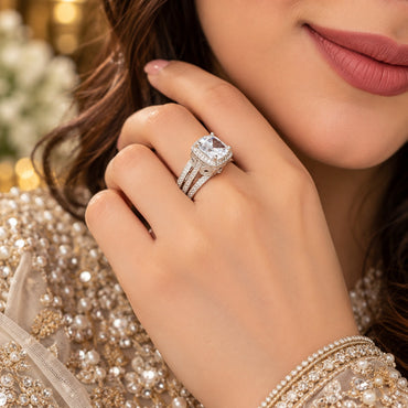 Silver Cushion Cut CZ Halo Art Deco Split Shank Bridal Ring lifestyle shot worn on model finger with pearl embroidered bridal outfit in background showing large cushion-cut white CZ solitaire in square micro-pave halo with Art Deco triple split shank and open scrollwork filigree infinity loop side motifs