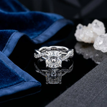 Silver-Tone Cushion-Cut CZ Solitaire Twisted Infinity Pavé Band Engagement Ring on black reflective surface with navy blue velvet fabric and white quartz crystal cluster backdrop
