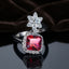 Silver Ruby Red Cushion CZ Halo Floral Crown Open Cocktail Ring on dark grey mirror surface with dark brown velvet drape backdrop