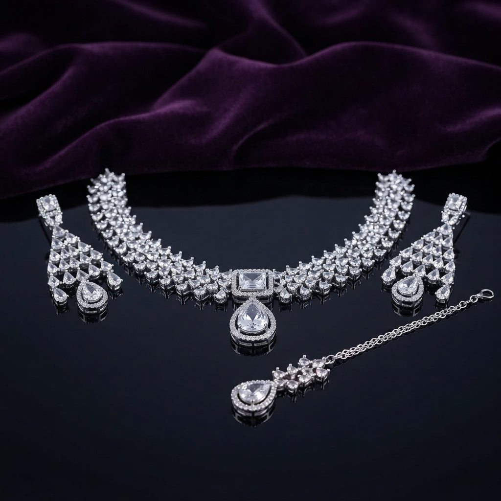 Silver CZ Cluster Choker Earrings and Maang Tikka Bridal Set in Diamond White on dark mirror surface with purple velvet backdrop showing rhodium silver wide mixed-cut white CZ cluster choker with white CZ square and pear pendant halo fan-drop earrings and maang tikka