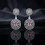 Silver CZ Concentric Orbit Double Disc and Pear Connector Drop Earrings in Emerald Green on dark mirror surface with charcoal satin backdrop showing rhodium silver pair with concentric cushion orbit stud white pear connector and large orbit disc pendant with round brilliant emerald green CZ centre solitaire