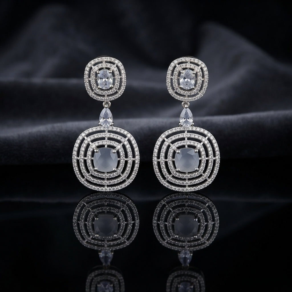 Silver CZ Concentric Orbit Double Disc and Pear Connector Drop Earrings in Navy Sapphire on dark slate surface with charcoal satin backdrop showing rhodium silver pair with concentric circular orbit stud white pear connector and large orbit disc pendant with oval navy sapphire blue CZ centre solitaire