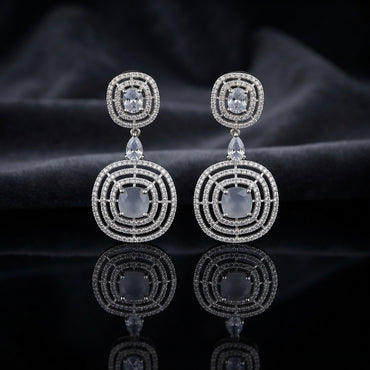 Silver CZ Concentric Orbit Double Disc and Pear Connector Drop Earrings in Navy Sapphire on dark slate surface with charcoal satin backdrop showing rhodium silver pair with concentric circular orbit stud white pear connector and large orbit disc pendant with oval navy sapphire blue CZ centre solitaire