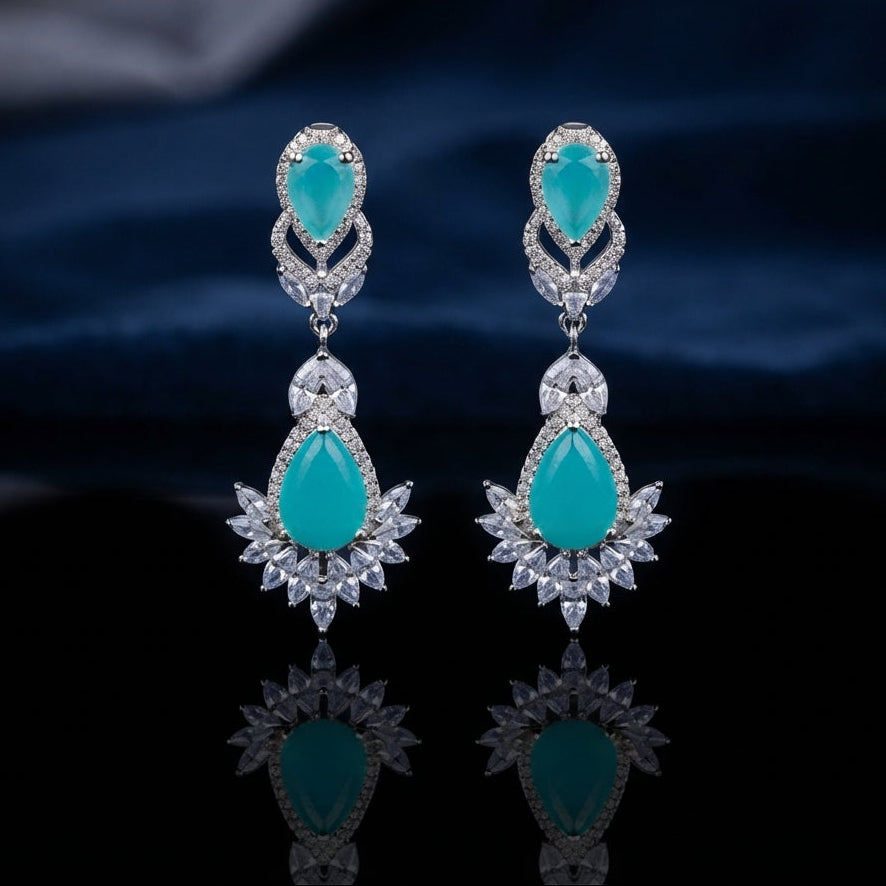 Silver CZ Double Teardrop Cabochon Lotus Fan Chandelier Earrings in Emerald Green pair on dark mirror surface with grey silk backdrop showing rhodium-plated small emerald green pear cabochon stud with white CZ pave halo infinity connector and large emerald green pear cabochon drop with white CZ pave halo and marquise CZ lotus fan crown with mirror reflection below