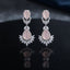 Silver CZ Double Teardrop Cabochon Lotus Fan Chandelier Earrings in Baby Pink pair on dark mirror surface showing rhodium-plated small rose quartz pear cabochon stud with white CZ pave halo infinity connector and large rose quartz pear cabochon drop with white CZ pave halo and marquise CZ lotus fan crown with mirror reflection below