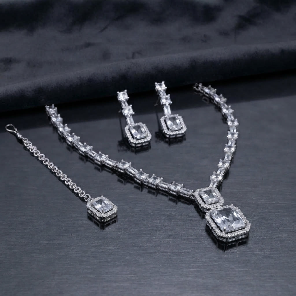 Silver CZ Emerald-Cut Baguette Tennis Necklace Earrings and Maang Tikka Set in Diamond White on dark charcoal satin surface showing rhodium silver full baguette CZ tennis necklace with double white CZ halo pendant matching drop earrings and maang tikka