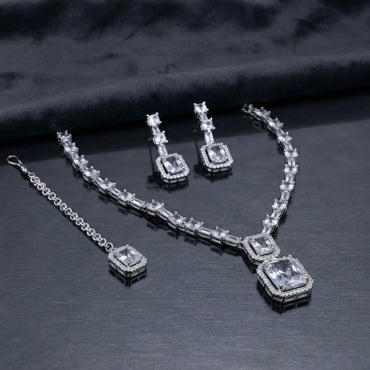 Silver CZ Emerald-Cut Baguette Tennis Necklace Earrings and Maang Tikka Set in Diamond White on dark charcoal satin surface showing rhodium silver full baguette CZ tennis necklace with double white CZ halo pendant matching drop earrings and maang tikka