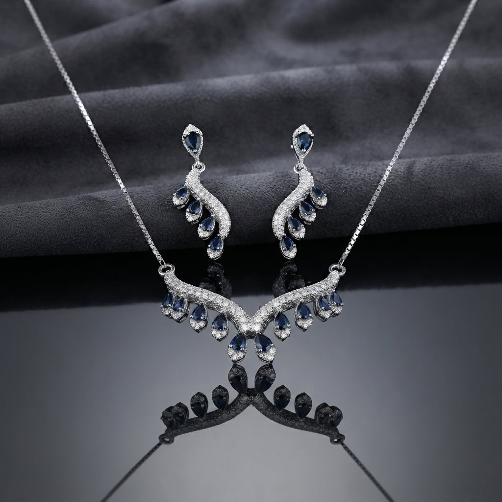 Silver Ruby Red CZ Feather Wing V-Bib Necklace and Drop Earrings Set flat lay on dark mirror black surface showing deep red ruby CZ graduating pear drops with white CZ micro-pavé feather wing body necklace and matching earrings with mirror reflection