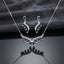 Silver Ruby Red CZ Feather Wing V-Bib Necklace and Drop Earrings Set flat lay on dark mirror black surface showing deep red ruby CZ graduating pear drops with white CZ micro-pavé feather wing body necklace and matching earrings with mirror reflection