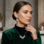 Silver White CZ Feather Wing V-Bib Necklace and Drop Earrings Set worn by model in emerald green velvet turtleneck showing all-white diamond illusion CZ feather wing V-bib necklace and matching feather wing drop earrings in warm grey editorial setting