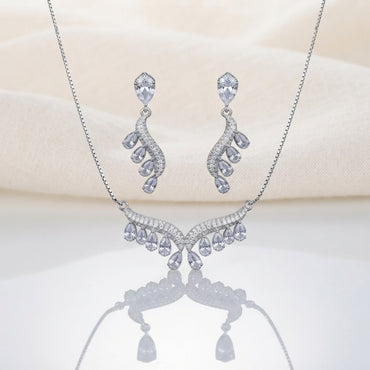 Silver White CZ Feather Wing V-Bib Necklace and Drop Earrings Set flat lay on ivory cream satin backdrop showing all-white diamond illusion CZ V-bib necklace with graduating pear CZ drops and matching feather wing drop earrings with reflection