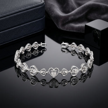 Silver-Tone CZ Filigree Heart Link Chain Bracelet on black mirror surface with navy leather jewelry box and charcoal grey silk fabric backdrop