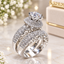 Silver CZ Halo Solitaire Bridal Ring Set 2 Piece side view on dark grey mirror surface with grey fabric backdrop showing cushion-cut CZ halo solitaire engagement ring stacked with wide infinity criss-cross CZ eternity band in rhodium silver-tone plating with mirror reflection below