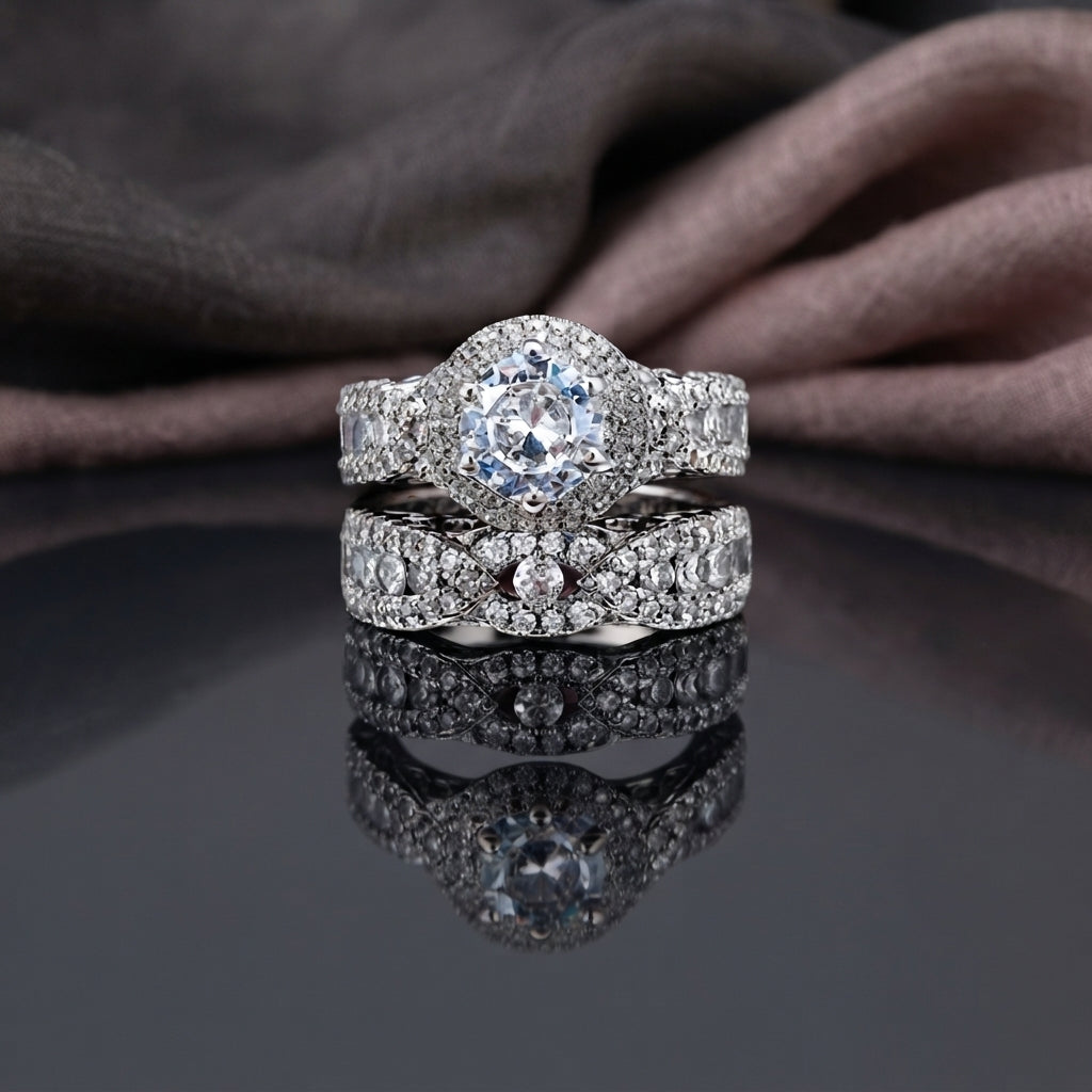 Silver CZ Halo Solitaire Bridal Ring Set 2 Piece angle view on marble surface with white flowers and gold jewellery box backdrop showing round brilliant CZ 6-claw solitaire ring stacked with wide triple-row micro-pave CZ band featuring open filigree arabesque scroll sides in rhodium silver-tone plating