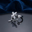 Silver CZ Marquise Flower and Bezel Round Chain Drop Open Adjustable Ring standing on dark grey mirror surface with deep navy teal satin velvet backdrop showing 4-petal marquise-cut white CZ flower top with round CZ centre connected by fine cable chain with small 4-petal CZ flower charm pendant to flat bezel-set round CZ opposite open arm in rhodium silver with dark oxidized shank and full mirror reflection below