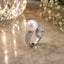 Silver-Tone CZ Pavé Panther Head & Pearl Bypass Open Cocktail Ring on cream marble surface with crystal bokeh light orb and white baby’s breath flowers backdrop