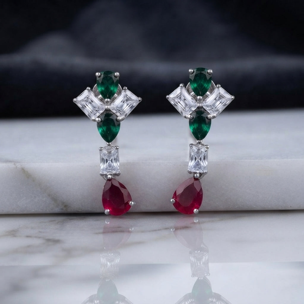 Silver CZ Pinwheel and Pear Ruby Drop Earrings in Rose Pink and Ruby colorway on dark mirror surface with charcoal satin backdrop showing rhodium silver princess CZ pinwheel cluster with rose pink oval and marquise accents baguette white CZ connector and vivid ruby red pear CZ drop