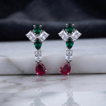 Silver CZ Pinwheel and Pear Ruby Drop Earrings in Rose Pink and Ruby colorway on dark mirror surface with charcoal satin backdrop showing rhodium silver princess CZ pinwheel cluster with rose pink oval and marquise accents baguette white CZ connector and vivid ruby red pear CZ drop