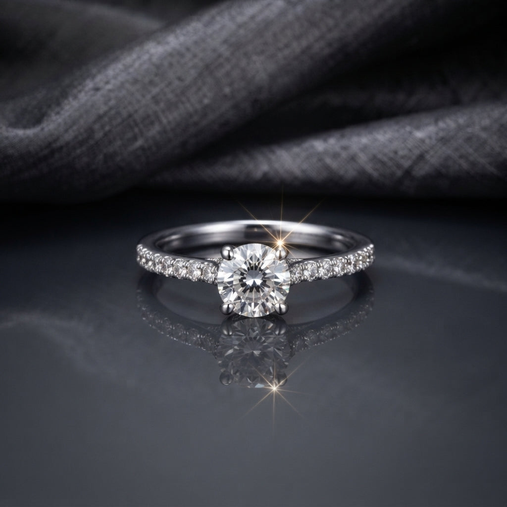 Silver CZ Solitaire Pavé Shoulder Engagement Ring front top view on dark grey mirror surface with grey fabric backdrop showing round brilliant CZ solitaire centre stone in 4-claw rhodium prong setting with single-row micro-pave CZ shoulder stones on slim tapered band with sparkle starburst effect and mirror reflection below